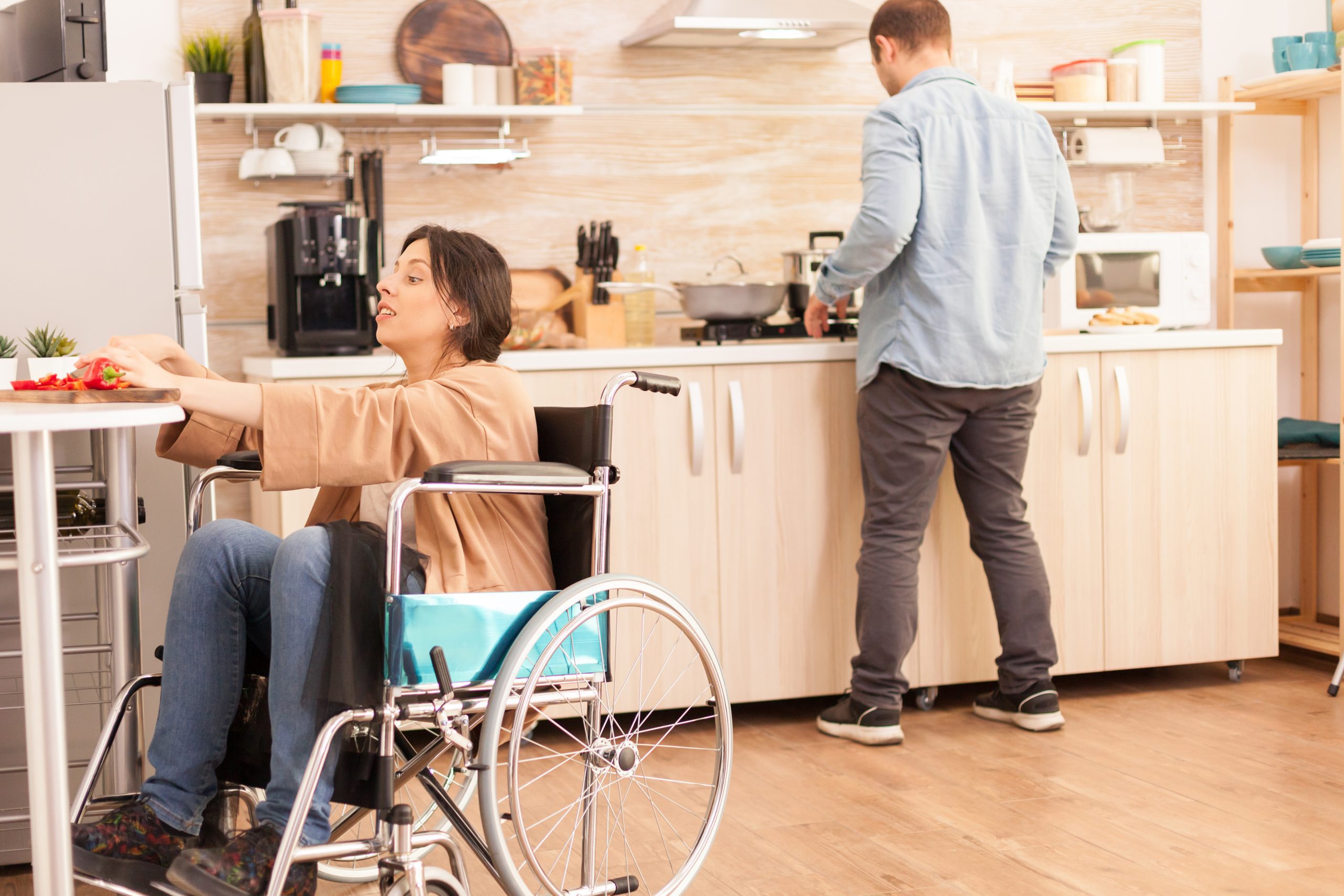 Woman in wheelchair prepares food with man also cooking in the background