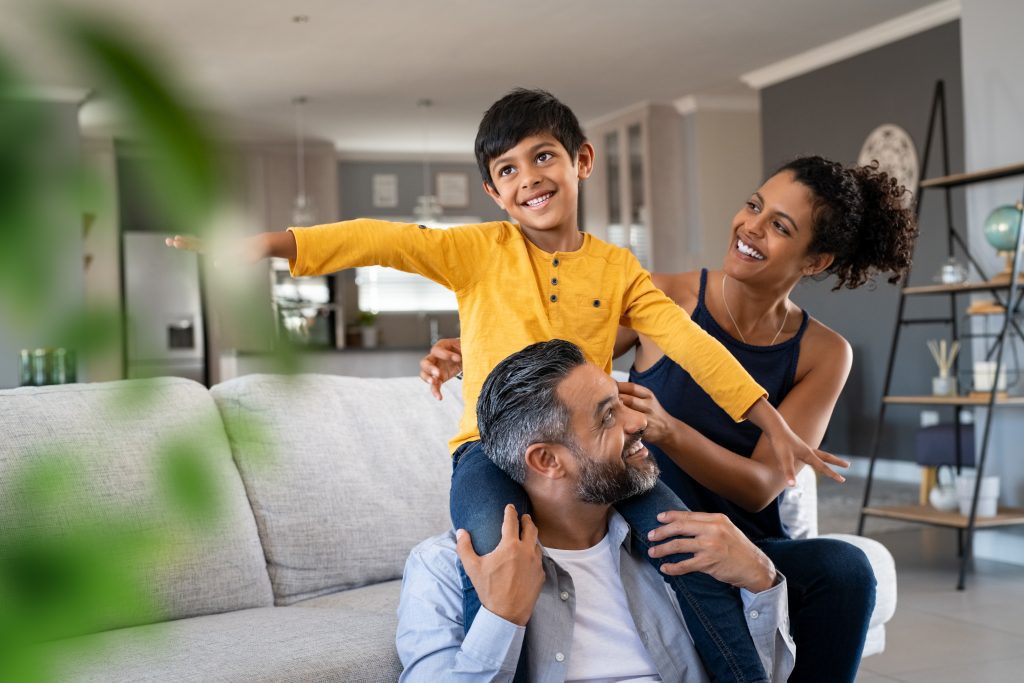 Cheerful little boy sitting on his Father's shoulders and playing at home