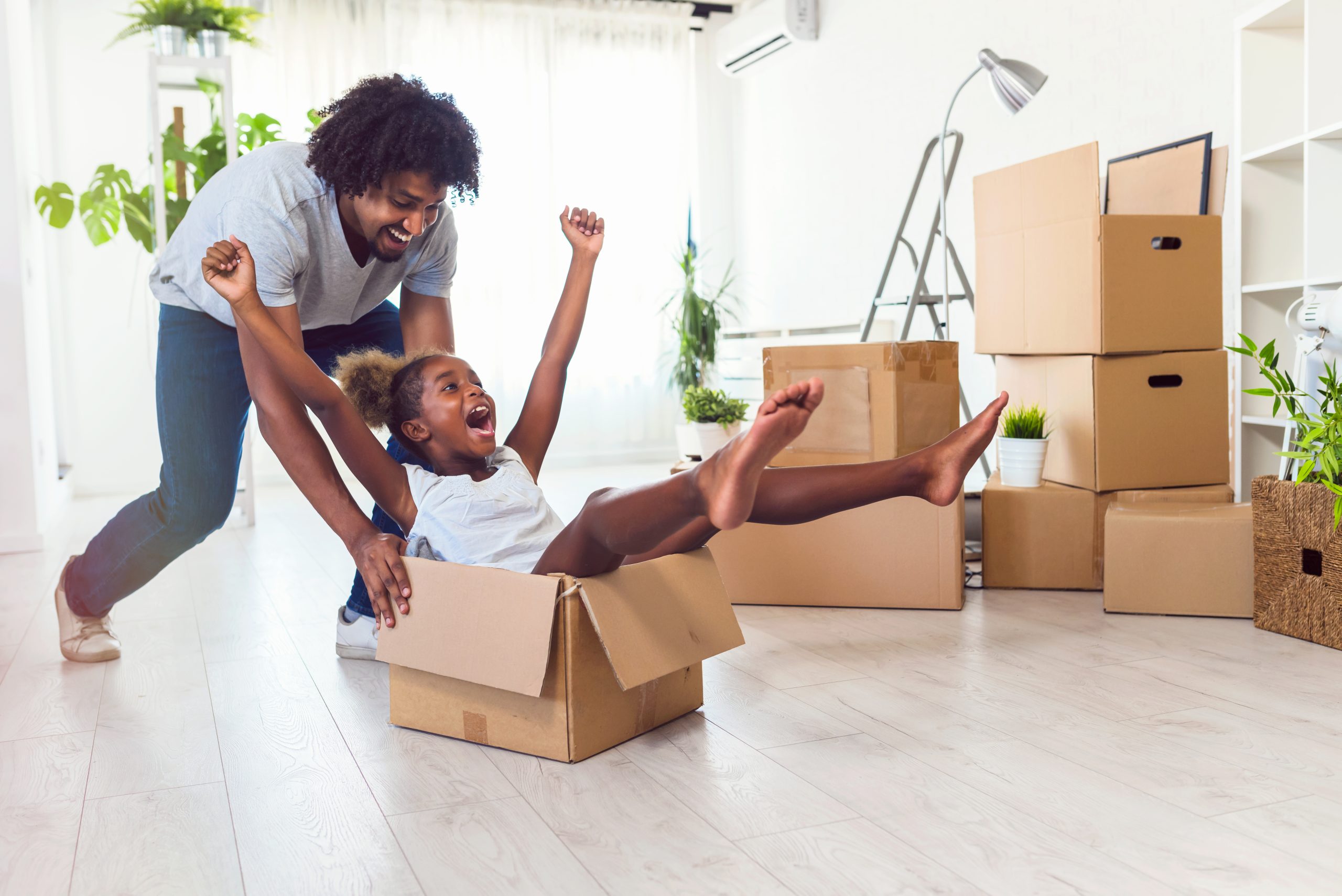 Father Pushing Cute Little Daughter Sitting Inside Of Carton Box, Smiling