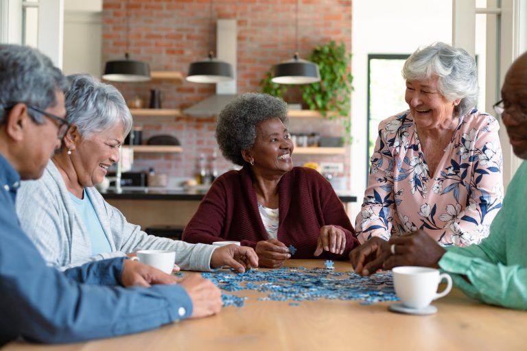 Group of elderly people sitting around a table, doing a jigsaw puzzle together and smiling