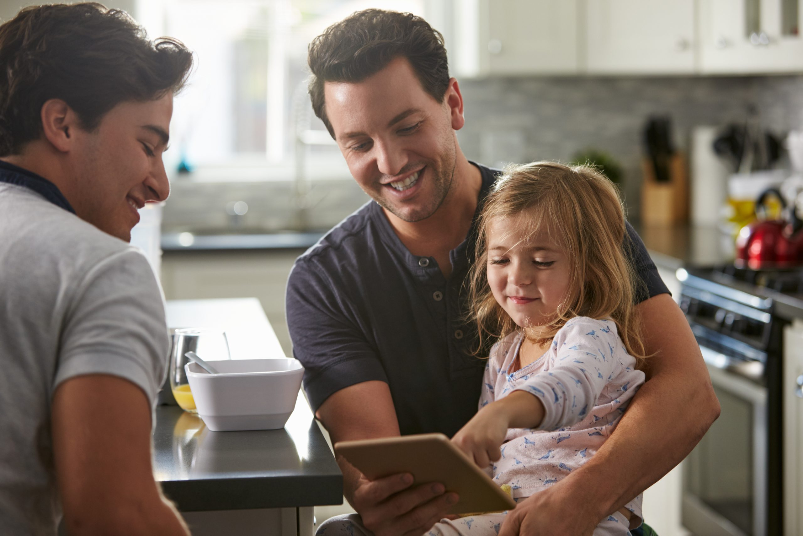 Male Gay Dads Use Tablet With Daughter In the Kitchen