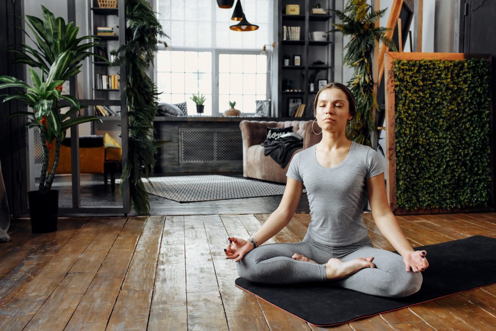 Woman meditating on yoga mat, sitting cross-legged with her eyes closed