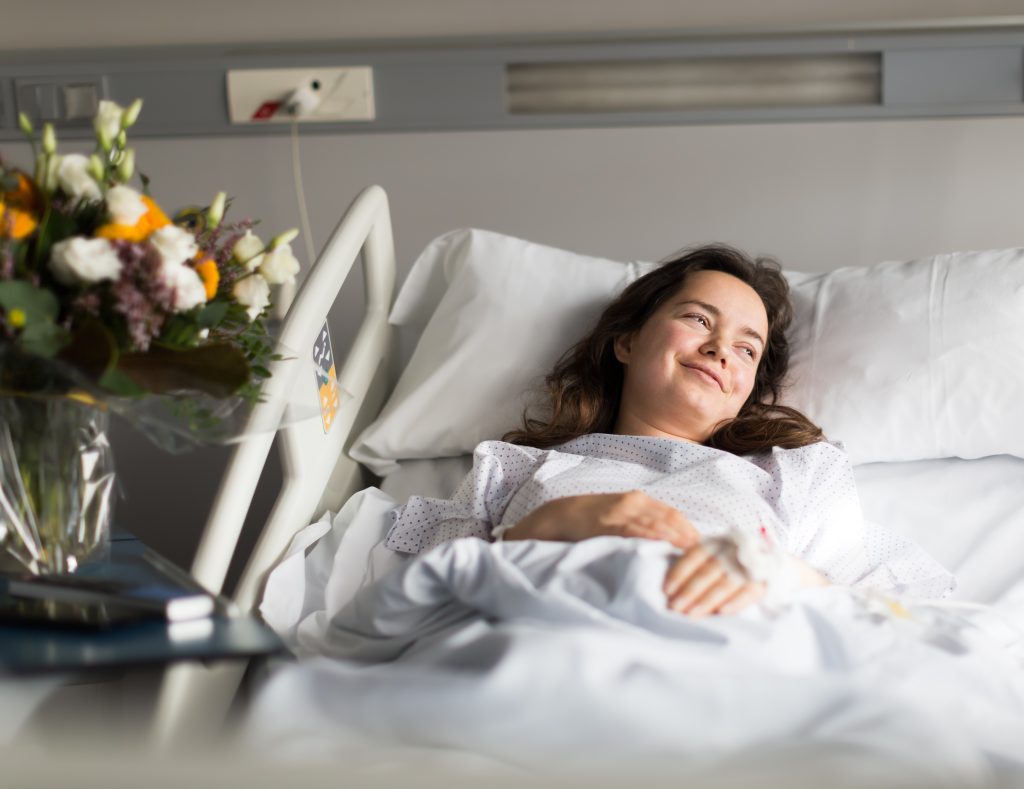 Woman laying in a hospital bed, smiling, after surgery