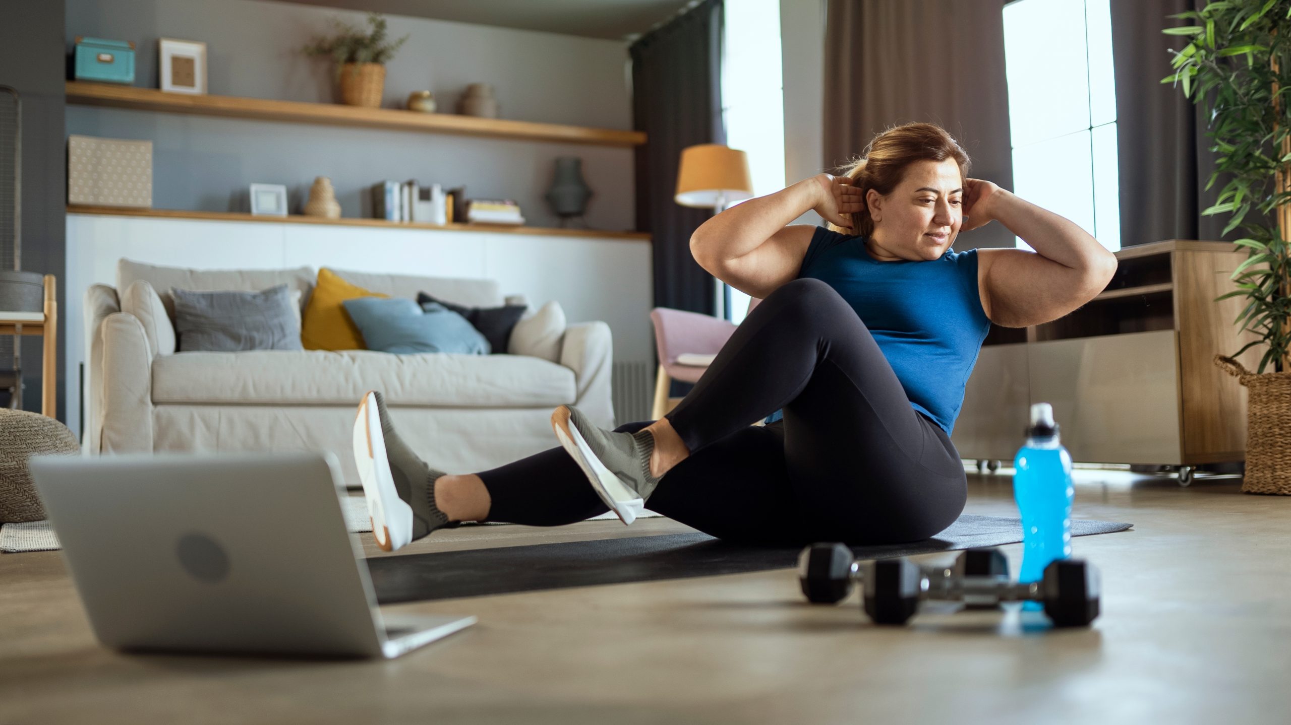 Woman doing crunches on exercise mat in front of her laptop at home