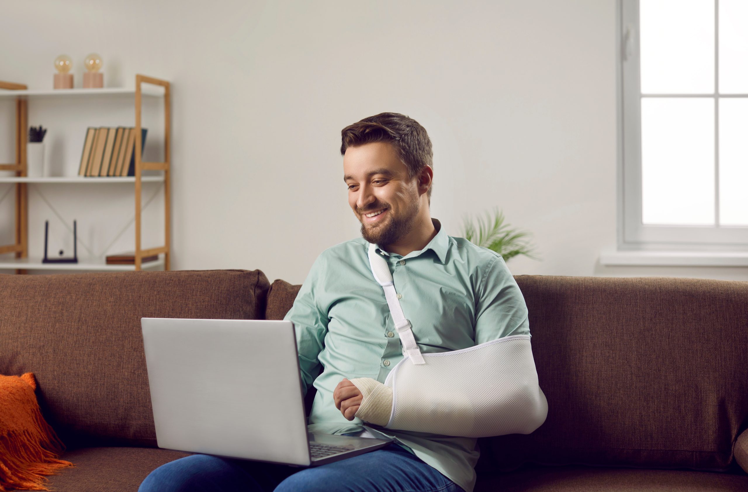 Man sitting on sofa on laptop with arm in sling