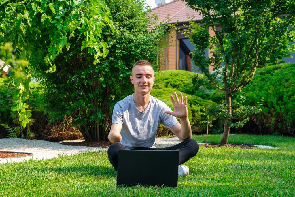 young guy smiling on laptop in the garden