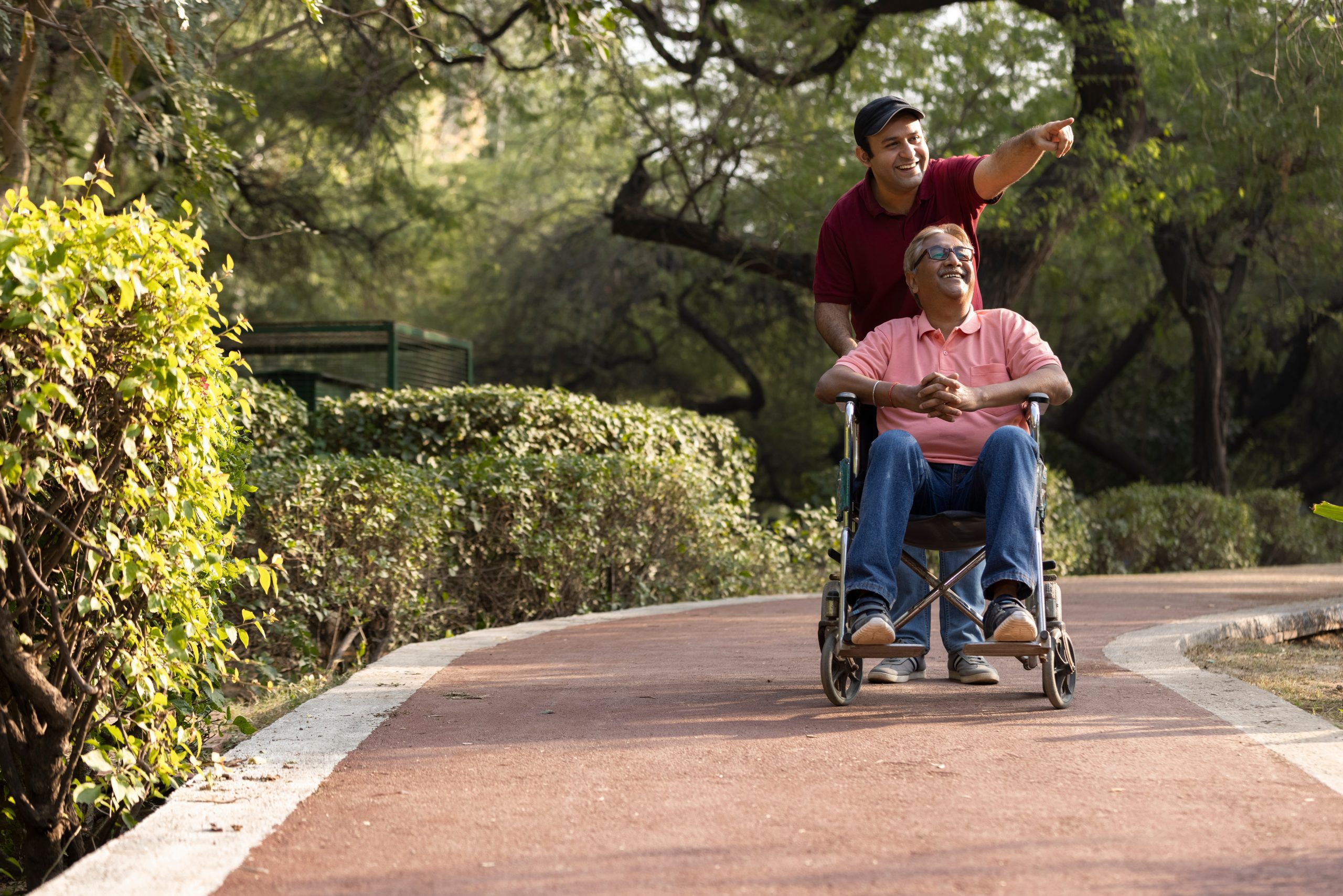 Man pushing an older man in a wheelchair down a path